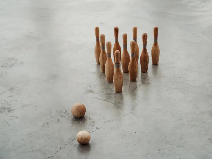 Wooden toy bowling set with ten pins and two balls on concrete floor