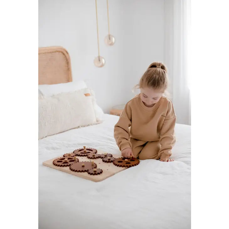 Child on bed playing with wooden gear construction play set