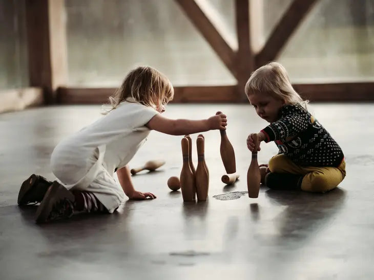 Children playing with wooden toy bowling set in room with concrete floor