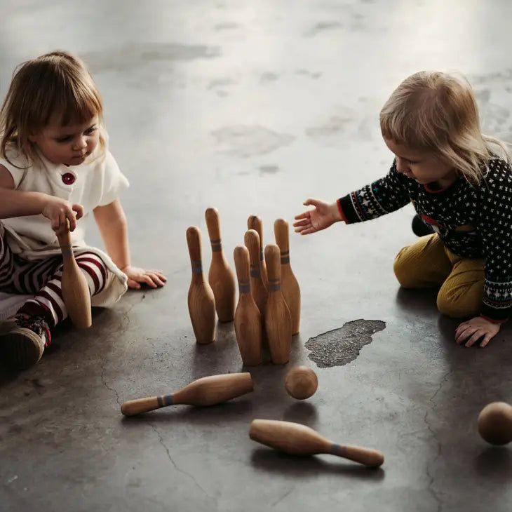 Children playing with wooden bowling set on concrete floor