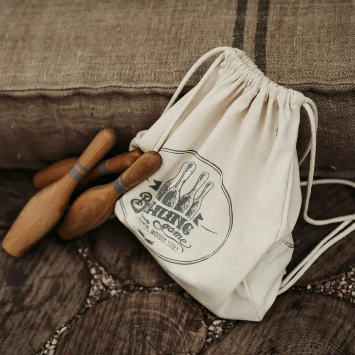 Three wooden toy bowling pins lay on cloth carrying sack