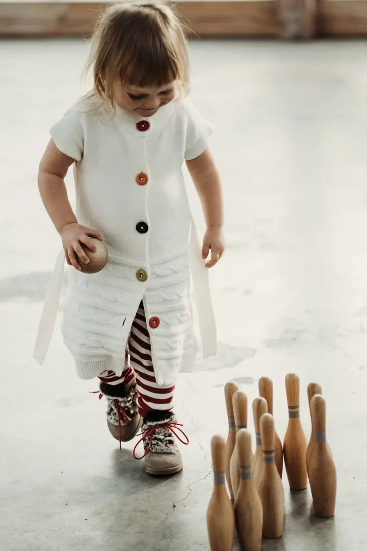 Girl holds toy wooden ball and walks next to wooden toy bowling pins