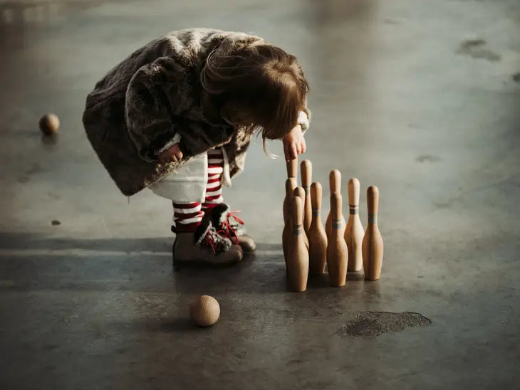 Toddler girl plays with wooden bowling pin set