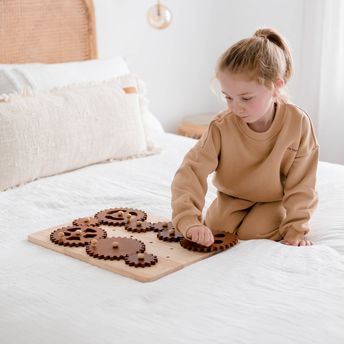 Child playing on bed with wooden gear construction set